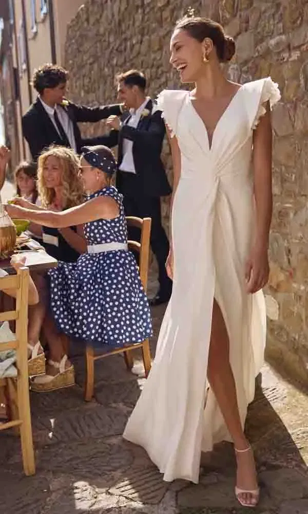 Elegantes Hochzeitskleid mit geraffter Taille, tiefem Ausschnitt und Beinschlitz in mediterraner Kulisse.