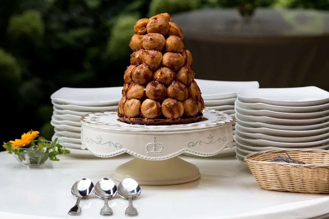 Croquembouche aus goldbraunen Windbeuteln mit Karamell, serviert auf einer verzierten Tortenplatte.