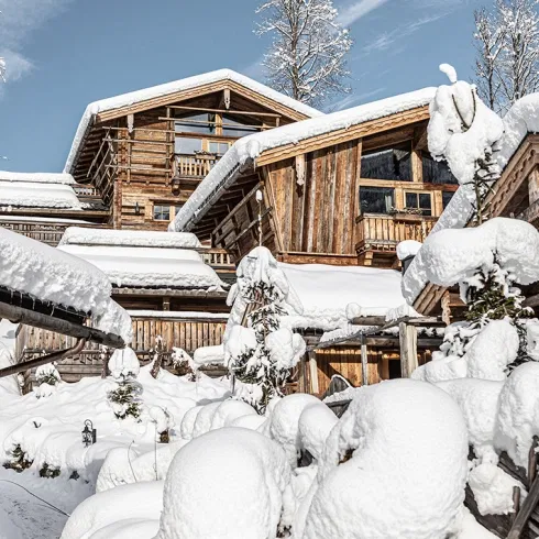 Verschneite Chalets des Bergdorfs Prechtlgut in winterlicher Berglandschaft unter blauem Himmel.