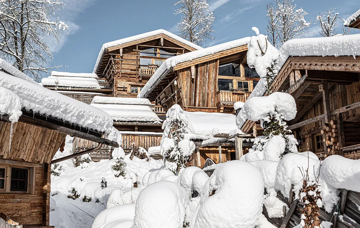 Verschneite Chalets des Bergdorfs Prechtlgut in winterlicher Berglandschaft unter blauem Himmel.