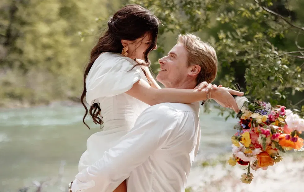 Glückliches Brautpaar in Umarmung bei einer Naturhochzeit am Flussufer – voller Liebe und Leichtigkeit.