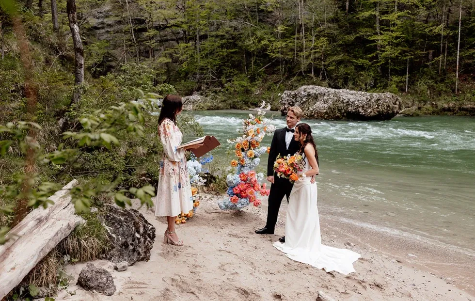 Freie Trauung in der Natur mit farbenfroher Blumendeko am Flussufer – ein emotionaler Hochzeitsmoment.