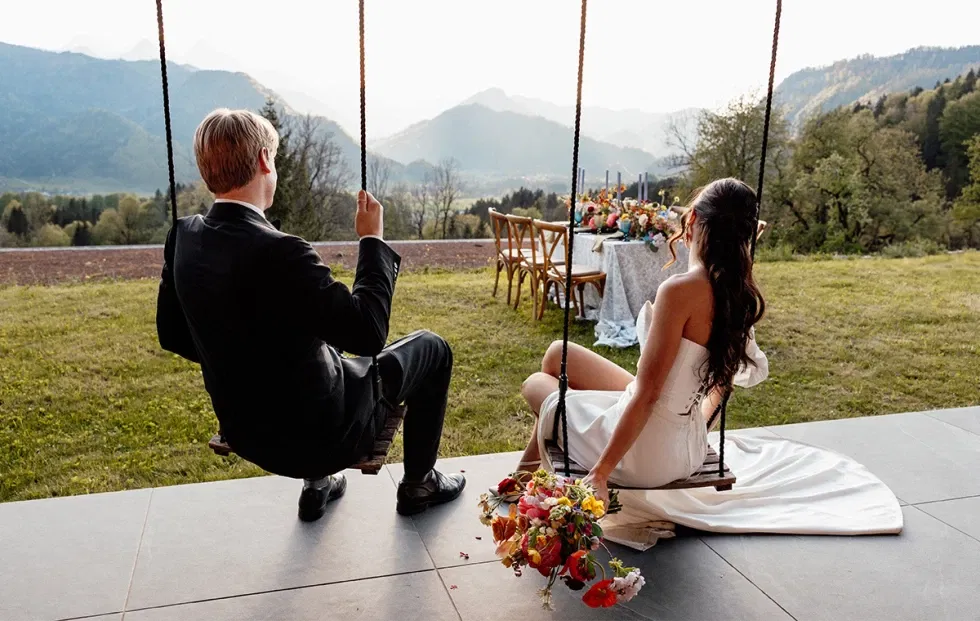 Braut und Bräutigam sitzen auf einer Schaukel mit Blick auf die Berge – ein Moment voller Ruhe und Romantik.