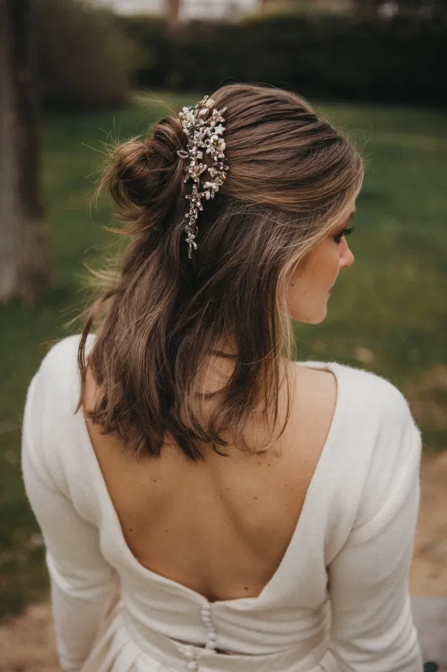 Braut von hinten mit halb offen gesteckter Frisur und floralem Haaraccessoire im Park.