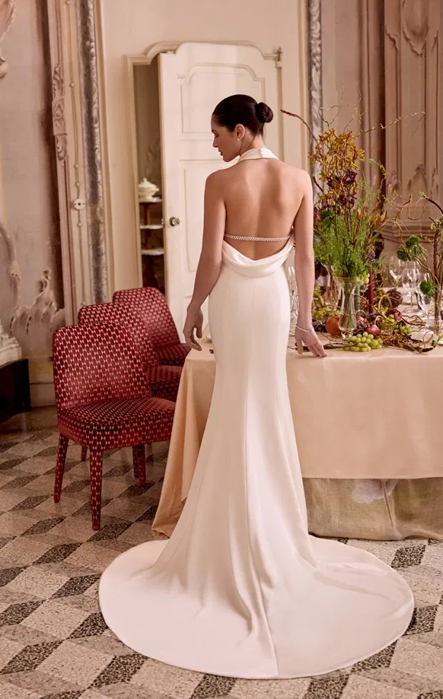 Elegantes Brautkleid mit tiefem Rückenausschnitt, drapiertem Stoff und langer Schleppe in einem historischen Raum.