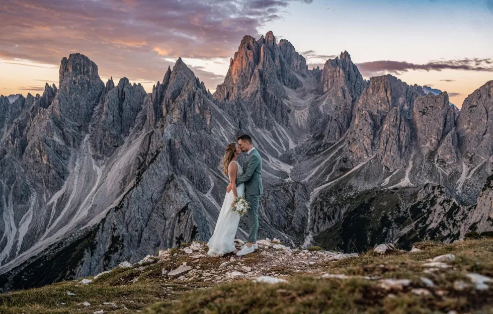 Ein Brautpaar küsst sich auf einem Bergplateau, umgeben von den dramatischen Felsformationen der Dolomiten im Abendlicht.