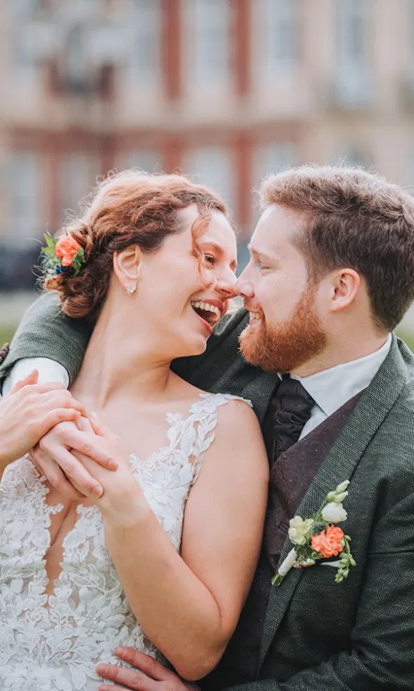 Verliebtes Brautpaar hält sich eng umschlungen und lacht einander strahlend an.