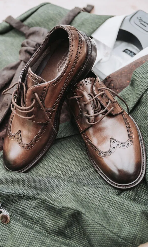 Braune Lederschuhe liegen auf dem grünen Anzug des Bräutigams, kombiniert mit Weste und Hemd.