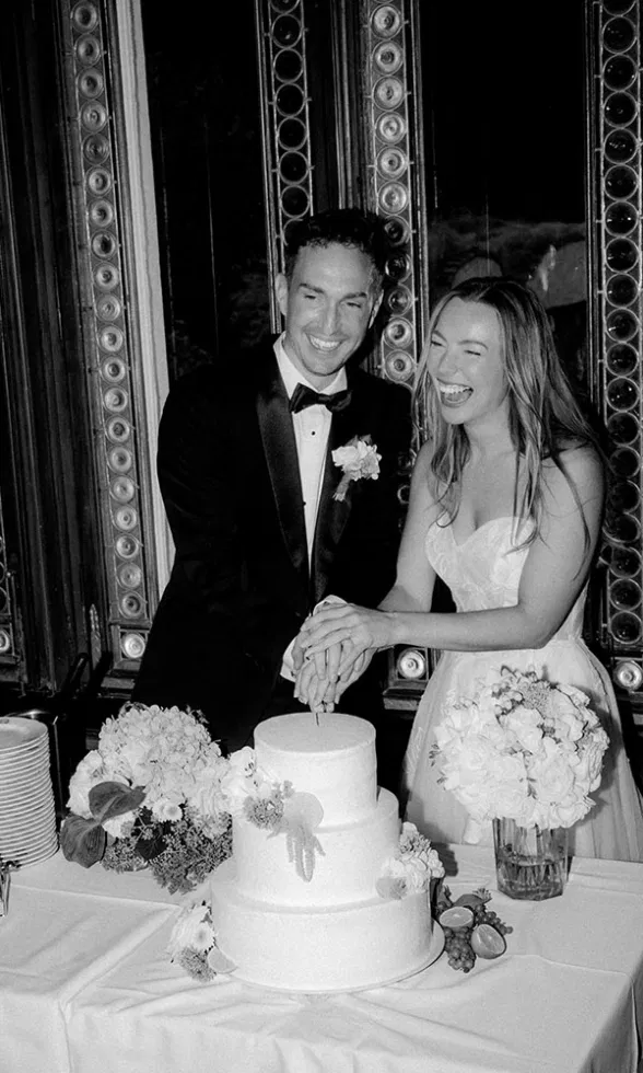 Schwarz-weiß Aufnahme des Brautpaares beim gemeinsamen Anschneiden der Hochzeitstorte, lachend und gelöst.