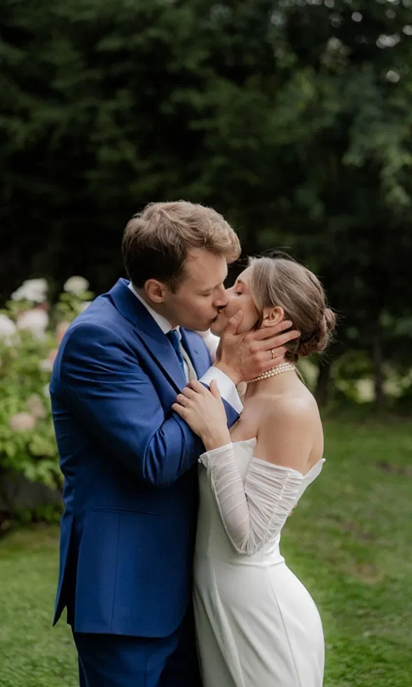Inniger Hochzeitskuss im Grünen: Braut und Bräutigam umarmen sich liebevoll inmitten einer natürlichen Gartenkulisse.