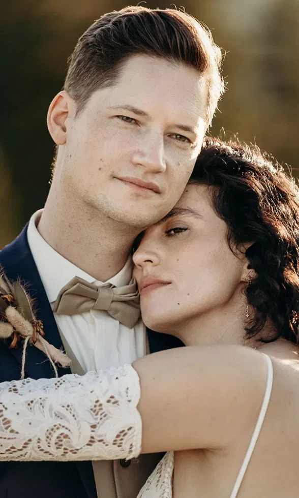 Nahaufnahme eines Brautpaares in inniger Umarmung, die Braut lehnt sich vertrauensvoll an den Bräutigam, warmes Licht unterstreicht die emotionale Stimmung.