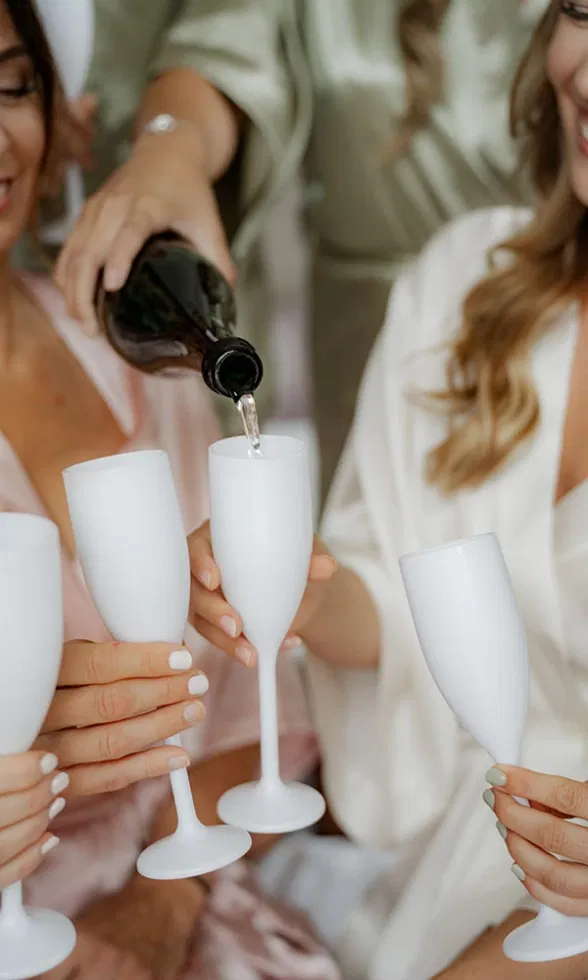 Getting-Ready-Moment mit Braut und Freundinnen: Sekt wird in weiße Gläser eingeschenkt, entspanntes Anstoßen vor der Hochzeit.