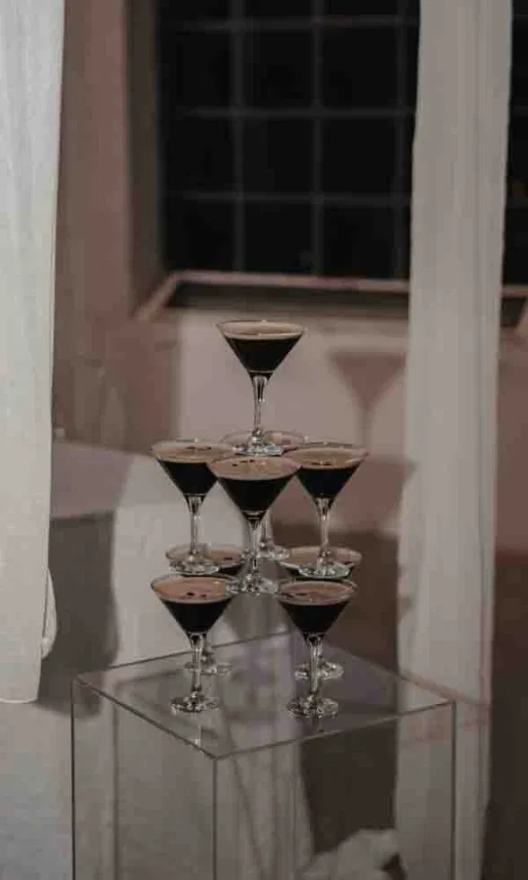 Gestapelte Espresso-Martini-Gläser auf einem transparenten Podest, stilvoll arrangiert in einem modernen, eleganten Hochzeitsambiente.