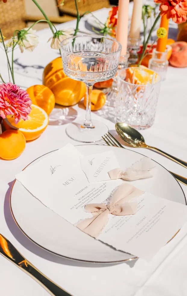Elegantes Gedeck mit Menükarte und Schleifen, Kristallglas und Zitrusdeko auf weißer Festtafel