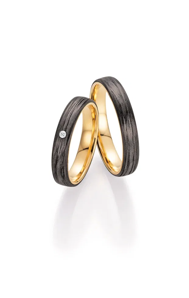 Fischer Trauringe mit Carbon-Oberfläche und warmem Goldkern, moderner Materialmix mit Diamantakzent.