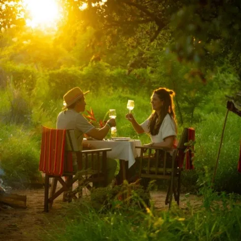 Romantisches Paar genießt ein privates Dinner im Grünen bei Sonnenuntergang in afrikanischer Naturkulisse.