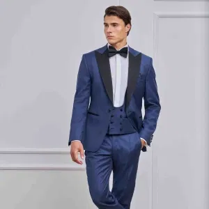 Eleganter Bräutigam-Anzug in Blau mit schwarzem Revers, Weste und Fliege, präsentiert in einem hellen Interieur – klassischer Hochzeitslook mit modernem Smoking-Charakter.