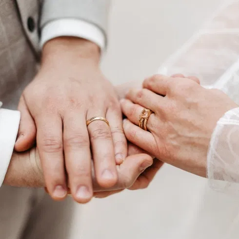 Ein Mann und eine Frau reichen sich die Hände. Ihre Eheringe sind zu sehen.