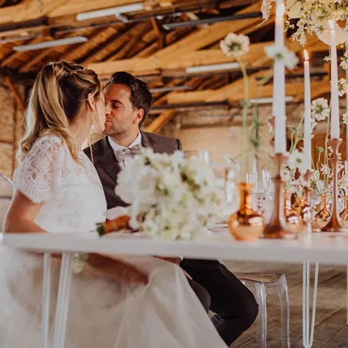Brautpaar sitzt an einer elegant gedeckten Tafel im historischen Sägewerk am Mondsee, umgeben von Kerzen, floraler Dekoration und rustikalem Industriecharme.
