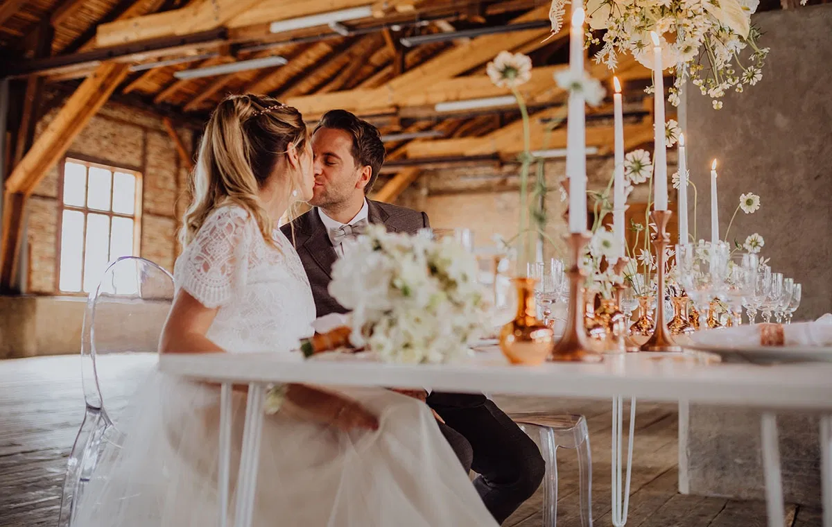 Brautpaar sitzt an einer elegant gedeckten Tafel im historischen Sägewerk am Mondsee, umgeben von Kerzen, floraler Dekoration und rustikalem Industriecharme.