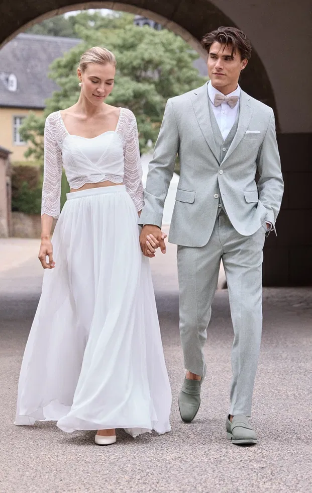 Mintgrüner Hochzeitsanzug mit Weste und Fliege, kombiniert mit heller Braut in zweiteiligem Spitzenlook – frischer Sommerstil.