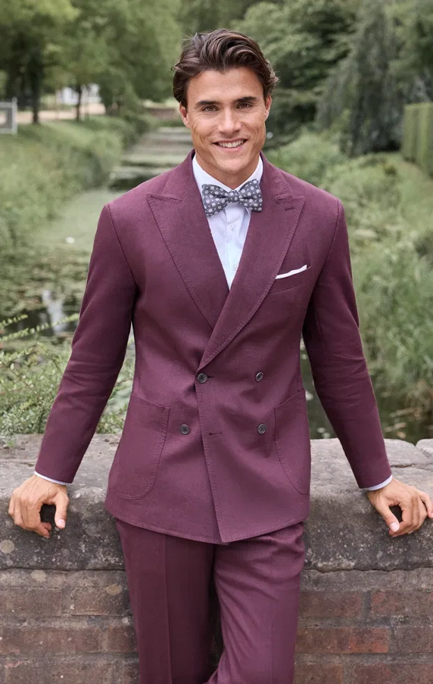 Bräutigam in beerenrotem Doppelreiher-Anzug mit gemusterter Fliege – klassisch-eleganter Hochzeitslook mit modernem Akzent.