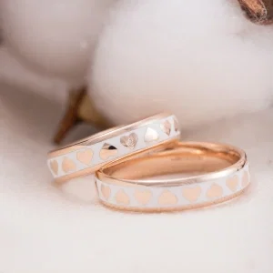 Zwei elegante Trauringe aus Roségold mit weißem Keramik-Inlay und eingearbeiteten Herzmotiven, einer mit kleinem Diamanten