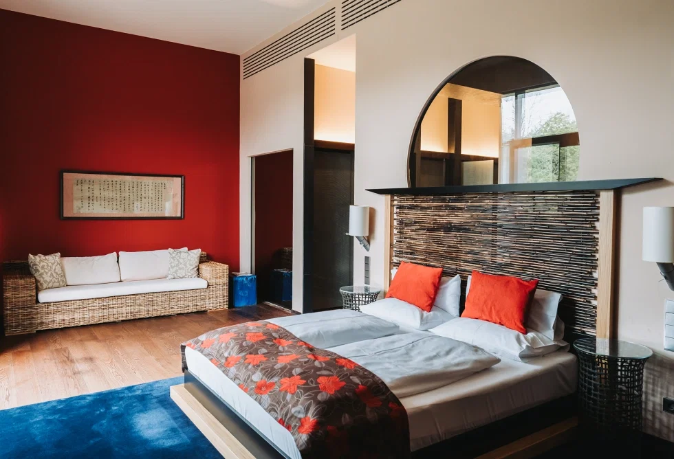Modern eingerichtetes Hotelzimmer mit Doppelbett, roten Akzenten, Holzdetails und stilvollem asiatisch inspiriertem Design