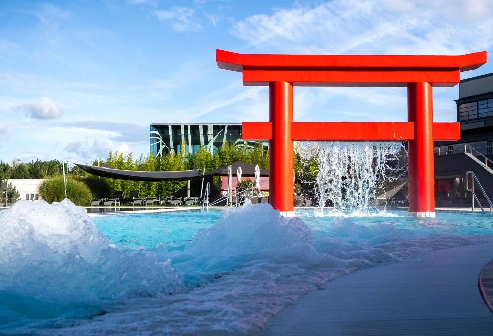 Außenpool des Linsberg Asia Hotels mit sprudelndem Wasser, rotem Torii-Tor als Blickfang und moderner Spa-Architektur im Hintergrund unter blauem Himmel