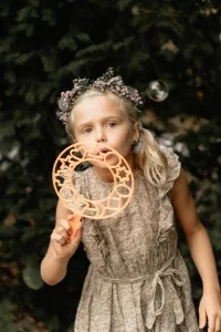 Mädchen mit Blumenkranz pustet konzentriert Seifenblasen und sorgt für verspielte Momente bei der Hochzeit.