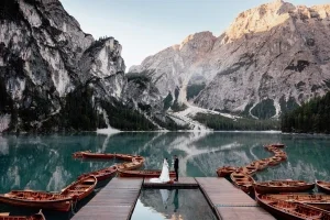 Braut und Bräutigam stehen auf einem Holzsteg vor türkisblauem Bergsee und imposanter Alpenkulisse, umgeben von kleinen Booten.