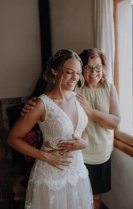 Mutter betrachtet ihre Tochter im Brautkleid voller Stolz und berührt sie liebevoll an den Schultern.