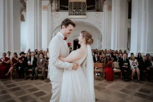 Frisch verheiratetes Paar umarmt sich strahlend vor den Gästen in einer eleganten Kirche nach dem Jawort.