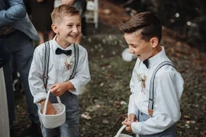 Zwei Ringträger lachen gemeinsam bei der Hochzeit und halten ihre Körbchen voller Blütenblätter bereit.