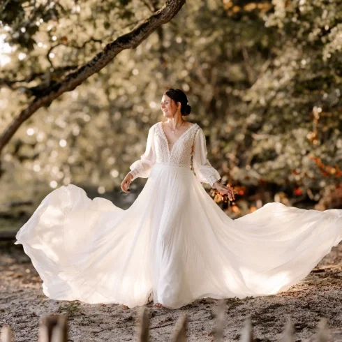 Braut im fließenden Boho-Brautkleid bei einem romantischen Brautshooting im Wald am Wasser.