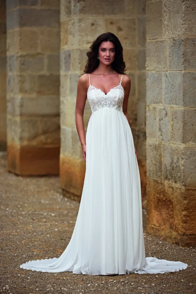 Dieses Empire-Brautkleid von Très Chic Avec Amour verzaubert mit zarten Spaghettiträgern, einem floral bestickten Oberteil und einem fließenden Chiffonrock, der luftig-leicht in eine Schleppe übergeht.