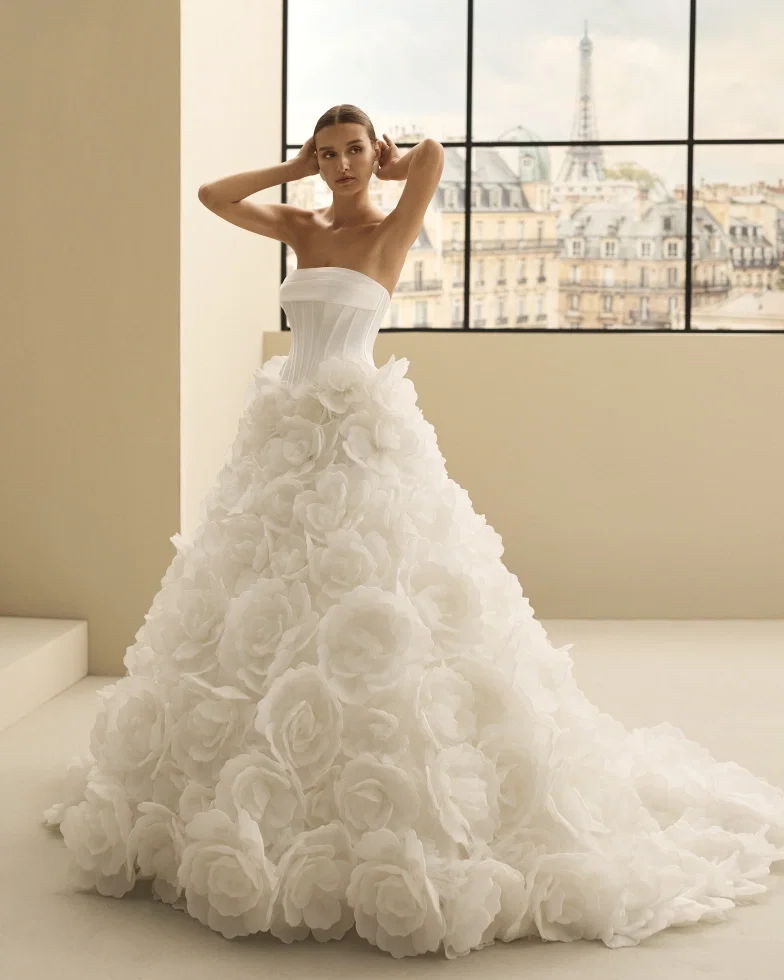 Bei diesem Prinzessinnen-Brautkleid „Nulet" von Rosa Clará Edition trifft ein trägerloses Corsagen-Oberteil auf einen üppigen Rock aus 3D-Blüten – ein romantisches Statement-Kleid mit Wow-Effekt.